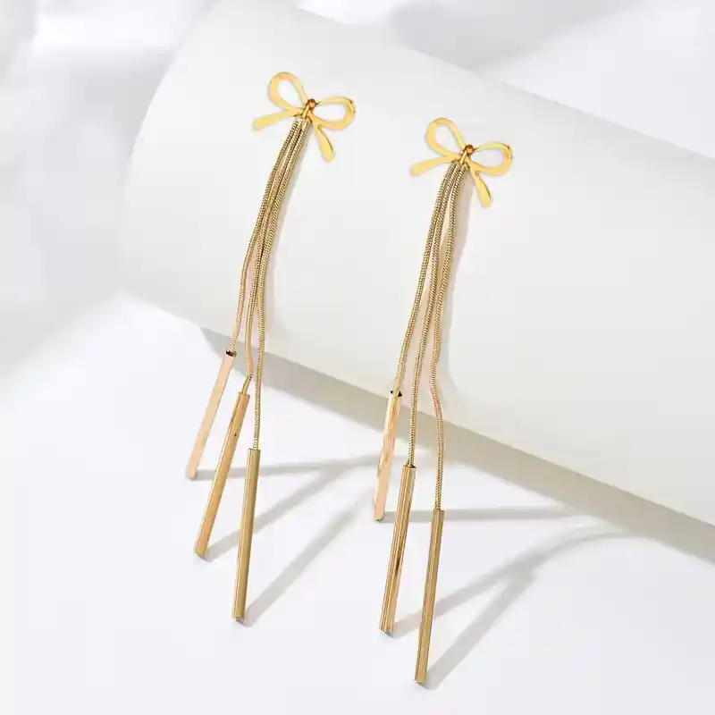 Χρυσά μακριά σκουλαρίκια 10 εκατοστών με σχέδιο φιόγκο και τρεις κρεμαστές λεπτές μπάρες σε λευκό φόντο.