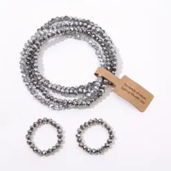 Σετ με πέντε ελαστικά βραχιόλια και δύο δαχτυλίδια από κρυστάλλινες χάντρες σε γκρι, μπλε και χρυσές αποχρώσεις.