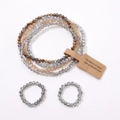 Σετ με πέντε ελαστικά βραχιόλια και δύο δαχτυλίδια από κρυστάλλινες χάντρες σε γκρι, μπλε και χρυσές αποχρώσεις.