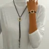 Σετ γυναικεία κοσμήματα με μακρύ κολιέ λάσο και βραχιόλι από μαύρο κορδόνι με σφυρήλατους χρυσούς κύκλους.