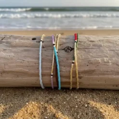 Minimal boho βραχιόλια με χάντρες περασμένα σε ξύλο στην άμμο με φόντο τη θάλασσα Chicbee