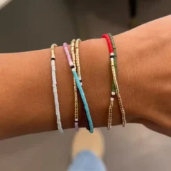 Γυναικείο χέρι που φοράει λεπτά boho χρυσά βραχιόλια με πολύχρωμες λεπτομέρειες Chicbee.gr